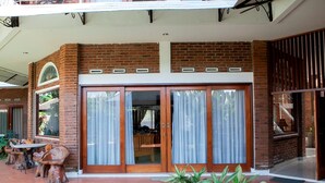A brick building with large glass doors and a patio area with wooden furniture. - RedDoorz Plus near Dago Pakar (Bandung)