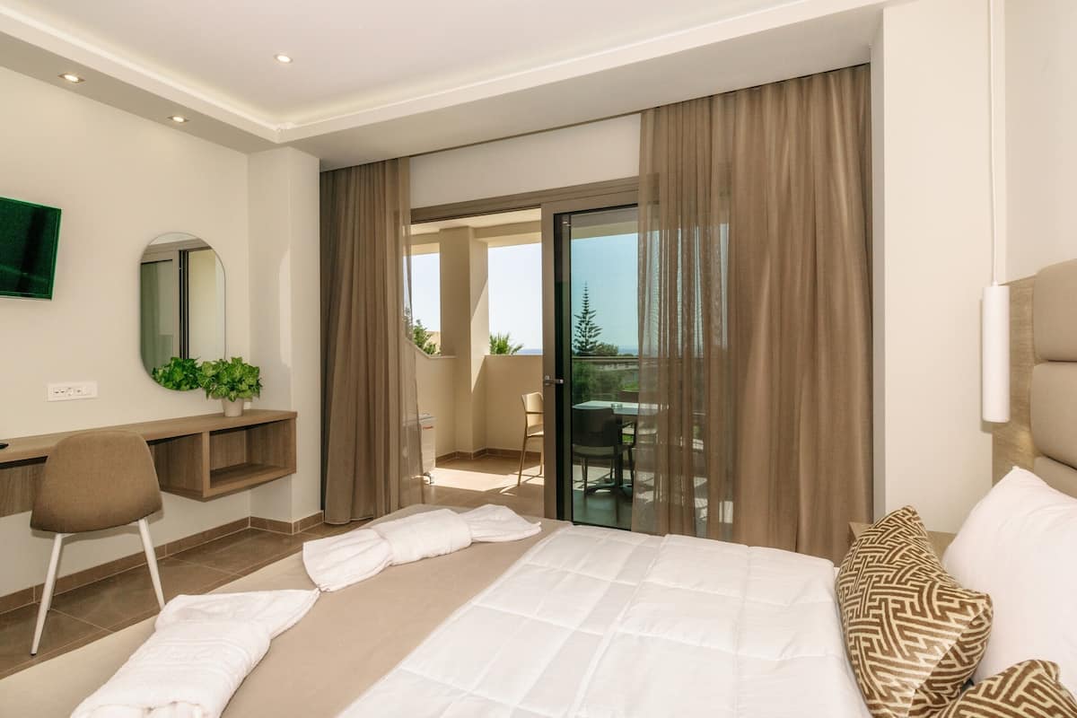 A hotel room with a bed, a desk, a chair, a TV, and a balcony with a view.