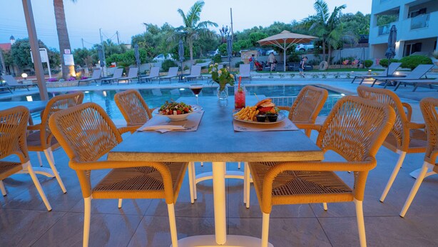 A poolside dining area with wicker chairs and a table set for two, overlooking a pool with lounge chairs and umbrellas. - Remezzo Apartments & Studios (Zakynthos)
