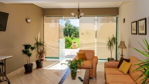 A living room with a sofa, coffee table, and potted plants. There is a television on the wall and a window with a view of the outdoors. - Remezzo Apartments & Studios (Zakynthos)