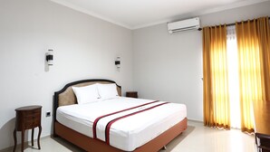 Ein Hotelzimmer mit einem großen Bett, einem Nachttisch, einer Klimaanlage und einem Fenster mit Vorhängen.
