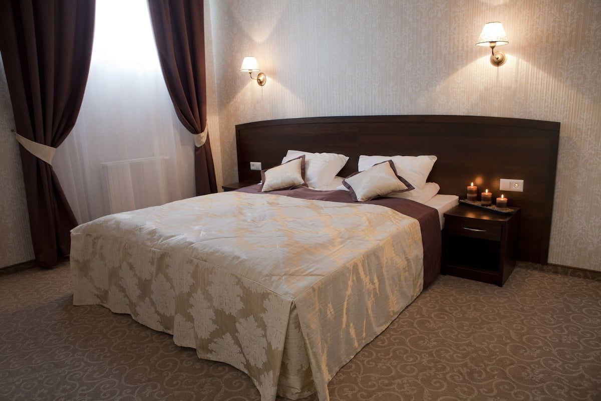 Une chambre d’hôtel avec un grand lit, deux lampes de chevet et une table de nuit avec des bougies.