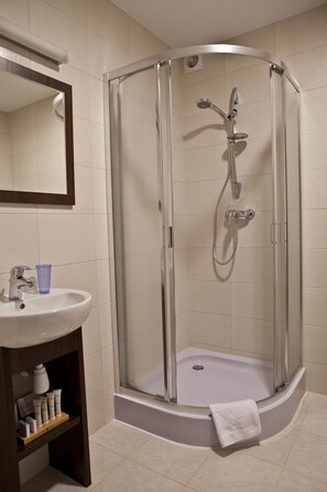 A corner shower with a glass door, a sink with a blue cup, and a white towel on the floor.