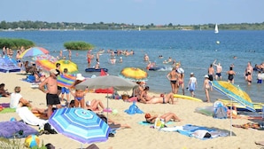Praia lotada com pessoas se bronzeando e nadando, guarda-sóis e cadeiras de praia.