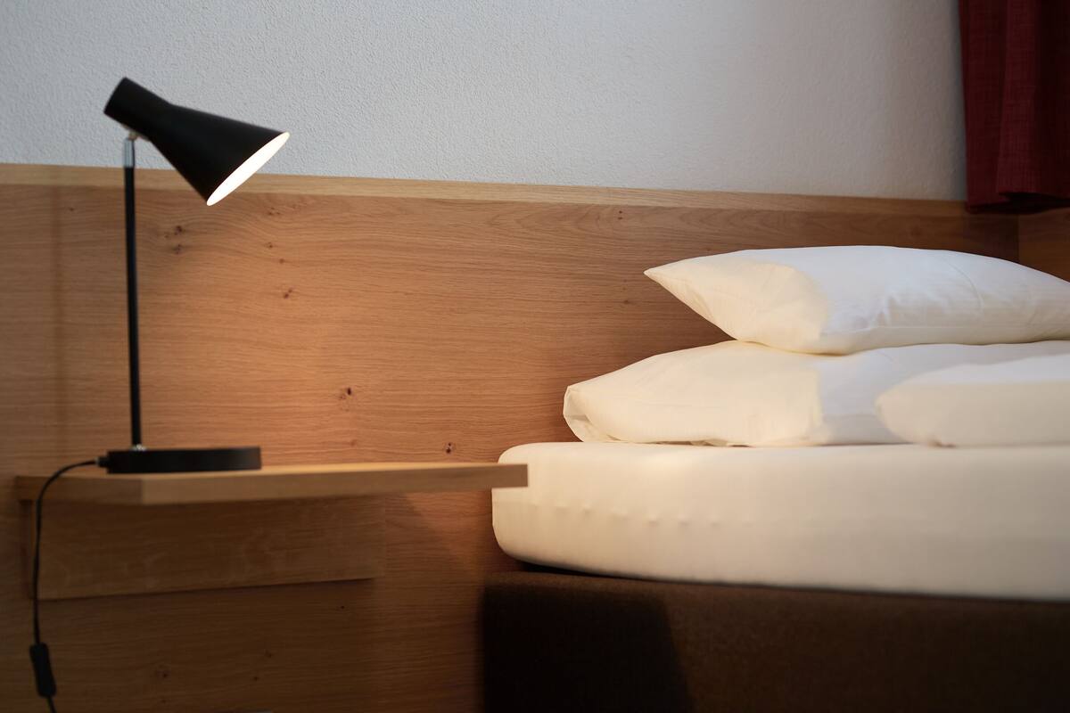 A neatly made bed with white bedding and a black floor lamp on a wooden nightstand.