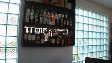 Zona de bar con estantes llenos de botellas de licor y bebidas en lata, con una ventana al fondo.