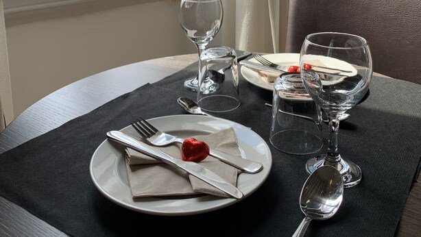 Una mesa puesta con platos, cubiertos y copas de vino, con vistas a un edificio histórico a través de una ventana abierta.