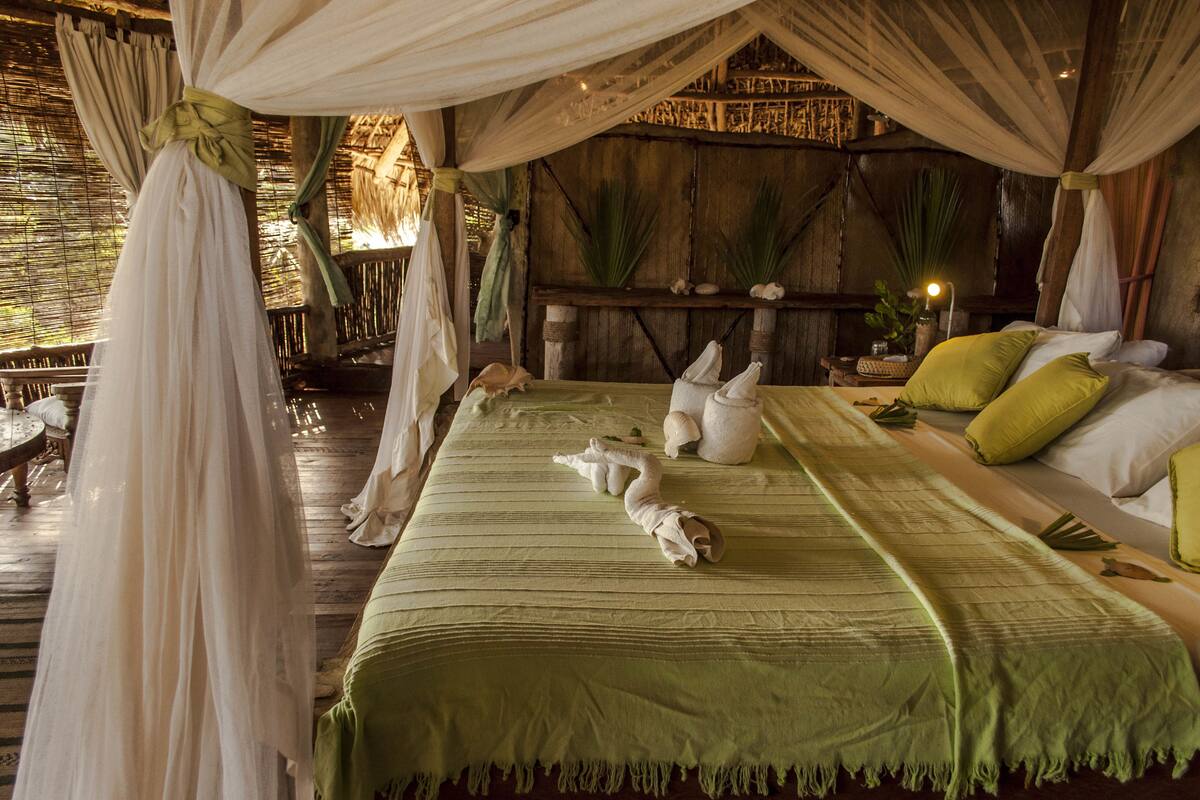 Una habitación con cama, colcha verde, almohadas blancas y dosel.