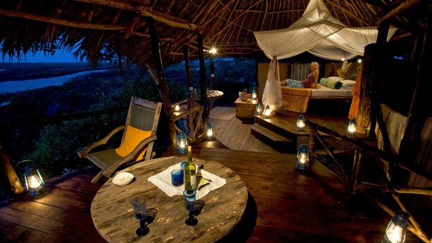 A wooden deck with a round table, chairs, and lanterns. There is a bed with a canopy and a view of the landscape. - H12 Delta Dunes Lodge (Kipini)