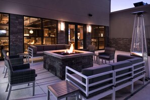 Un patio exterior con un brasero, asientos y vistas al interior.