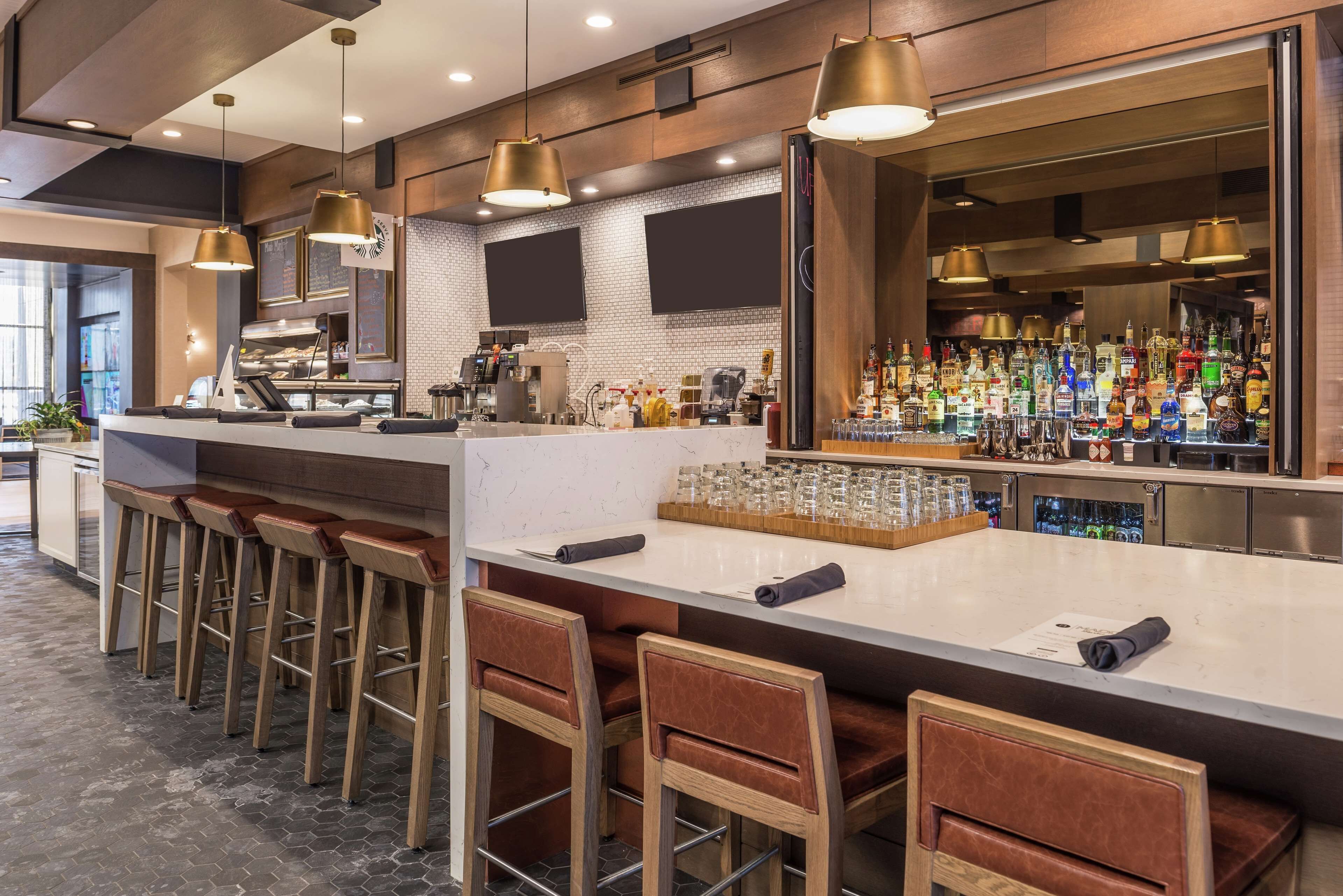 Zona de bar moderna con taburetes de madera, una barra con utensilios para coctelería y una amplia selección de licores.