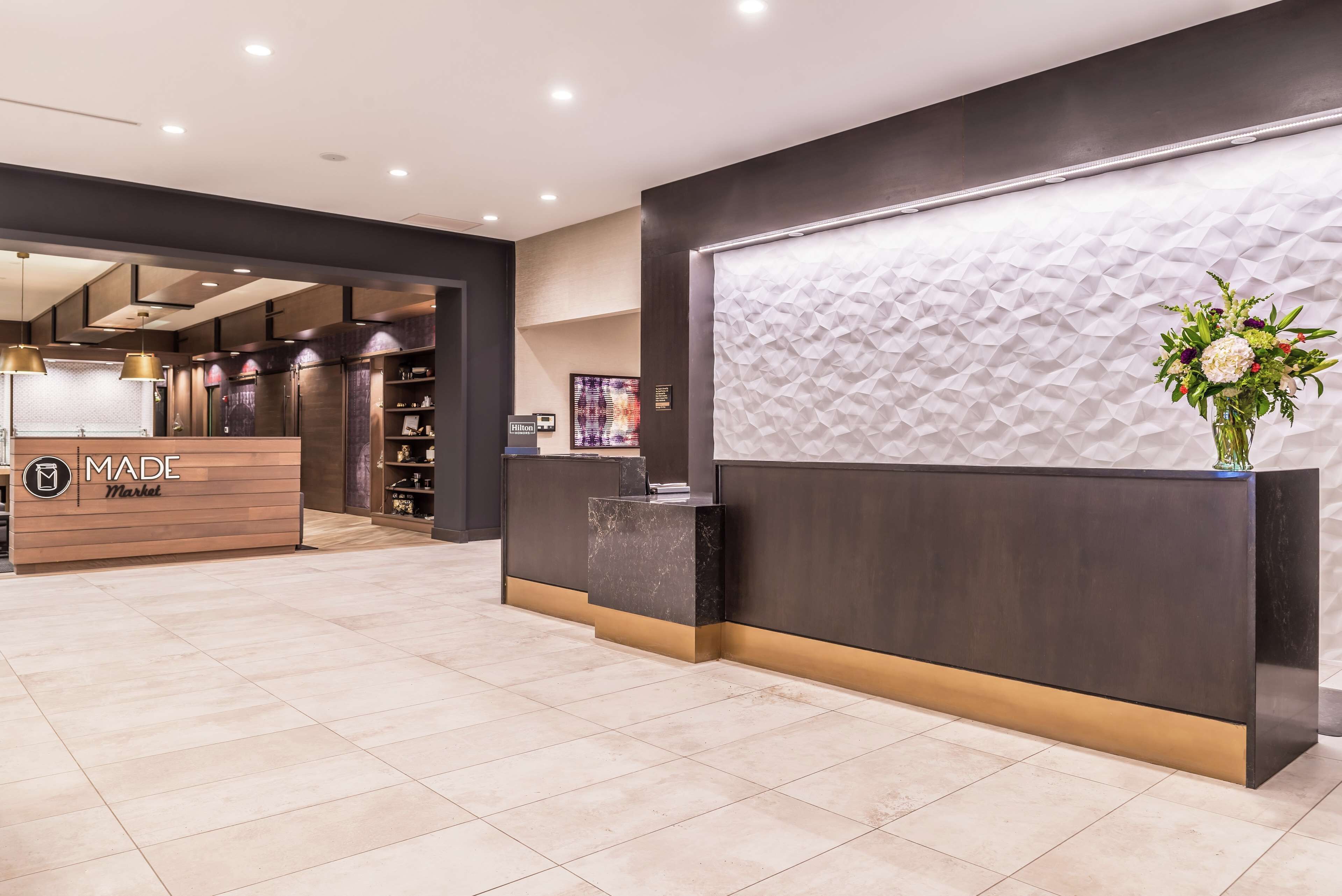 A hotel reception area with a modern design, featuring a reception desk, a 'Made Market' sign, and a decorative wall with a textured pattern.