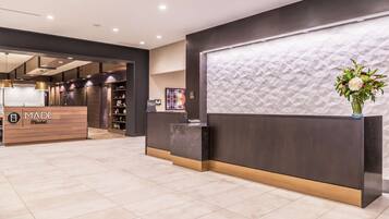 A hotel reception area with a modern design, featuring a reception desk, a 'Made Market' sign, and a decorative wall with a textured pattern.
