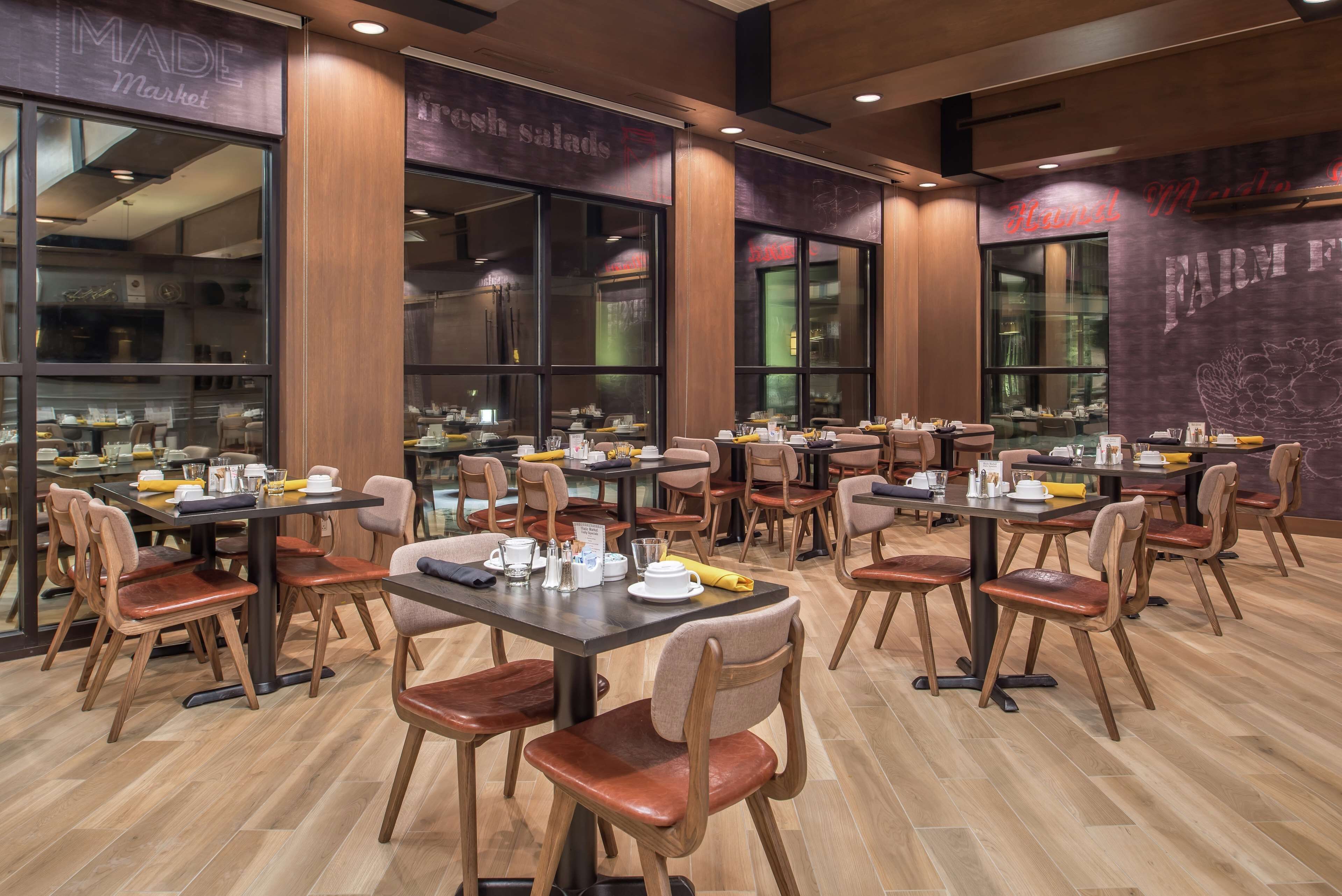 Een restaurant met meerdere tafels en stoelen, grote ramen en een houten vloer.