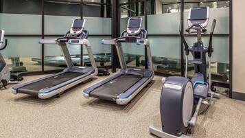 Drei Laufbänder und ein Crosstrainer in einem Fitnessstudio mit großen Fenstern und Teppichboden.