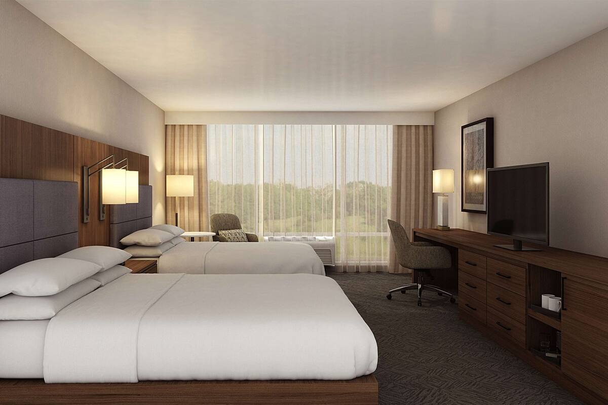 A hotel room with two beds, a desk with a TV, and a chair.