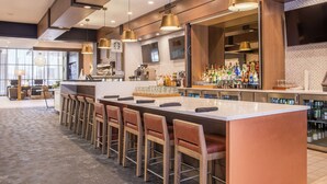 Un área de bar moderna con una barra alargada, varios taburetes y una gran variedad de botellas y vasos.