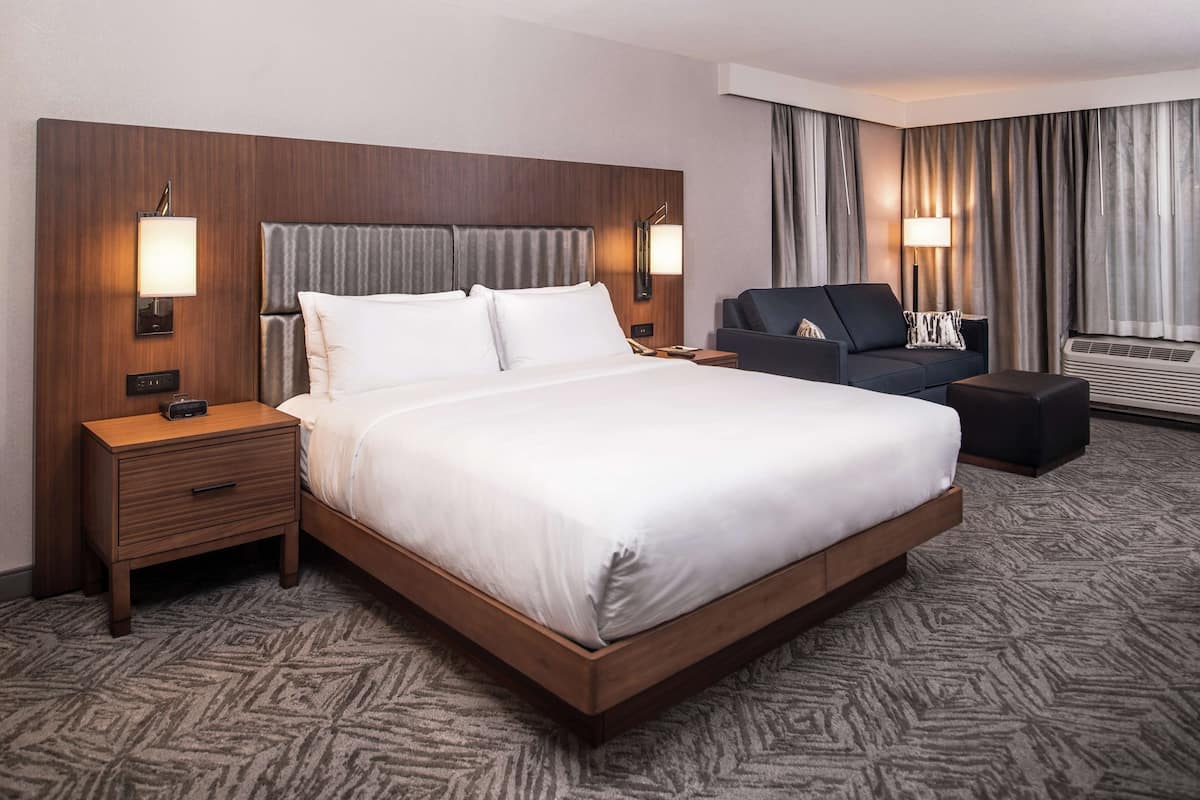 A hotel room with a large bed, a nightstand, a sofa, and a small table.