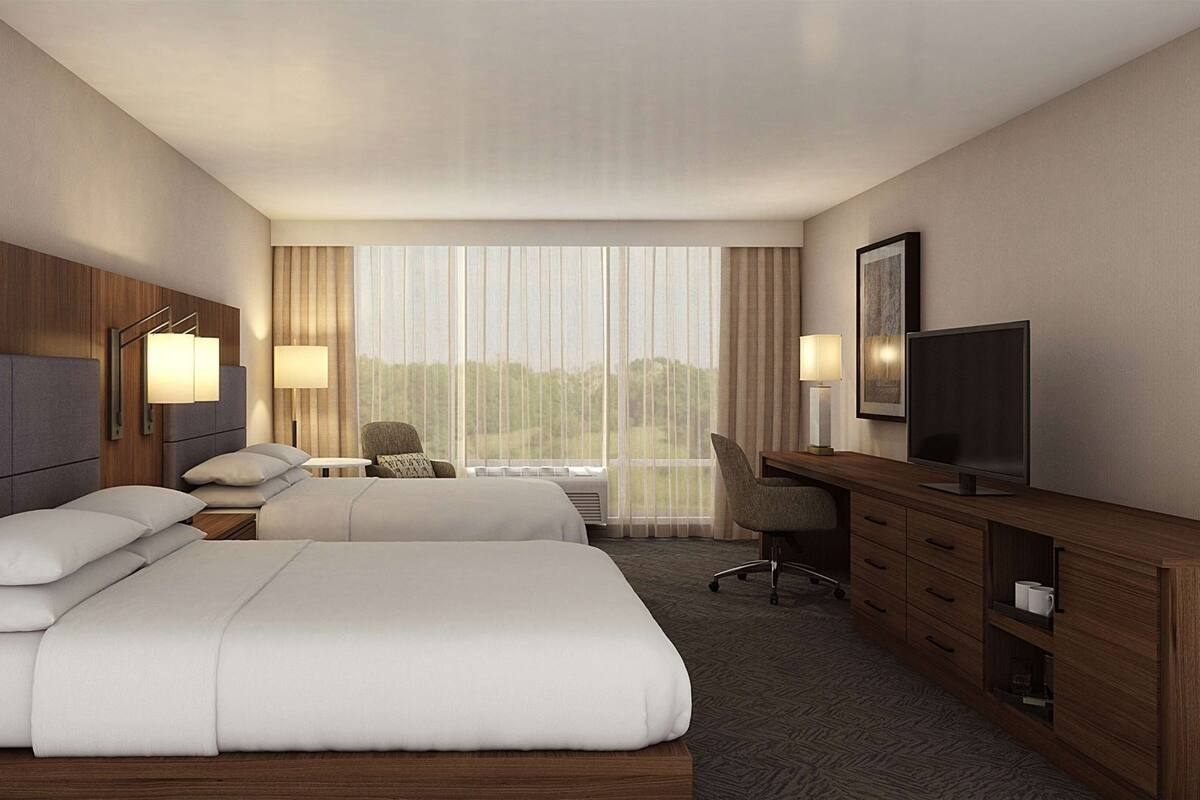 A hotel room with two beds, a desk, a chair, a TV, and a large window with curtains.