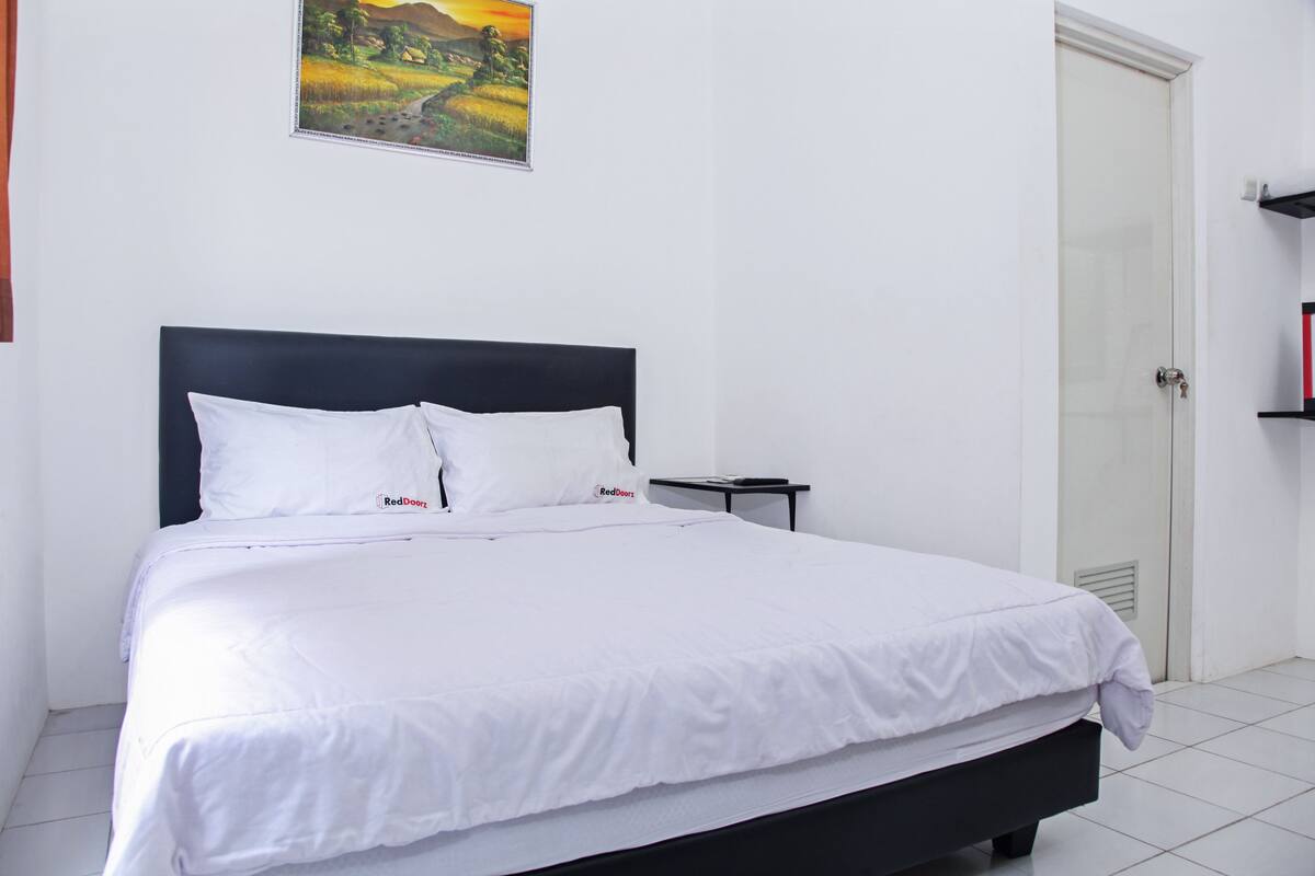 A neatly made bed with white linens, a black headboard, and a small bedside table with a lamp.