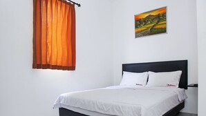 A bedroom with a black headboard, white bedding, and a painting of a landscape on the wall.