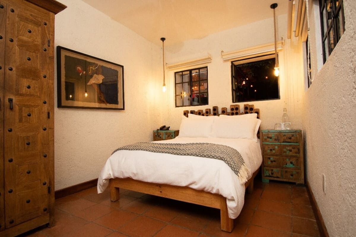 Une chambre à coucher avec un lit en bois, deux tables de chevet, une armoire en bois et un tableau encadré au mur.