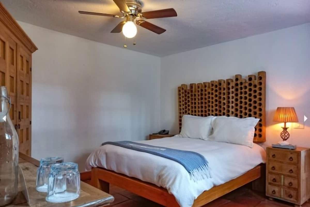 Une chambre à coucher avec un lit en bois, une table de chevet, une lampe et un ventilateur de plafond.