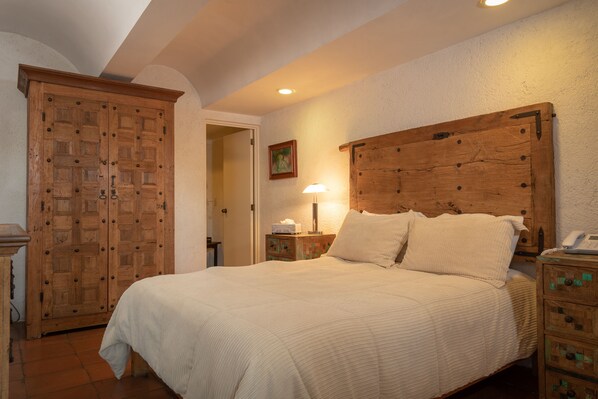 A bedroom with a large wooden bed, a wooden wardrobe, and a bedside table with a lamp.