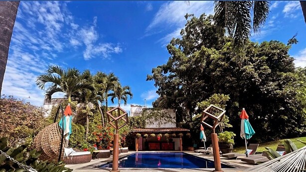 A pool area with lounge chairs, a hammock, and a small building with a tiled roof. - La Provence Restaurant & Boutique Hotel (Cuernavaca)