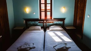 A room with two single beds, a window with a view, and wall-mounted lights. - Karnayo Traditional Houses (Kastellorizo)