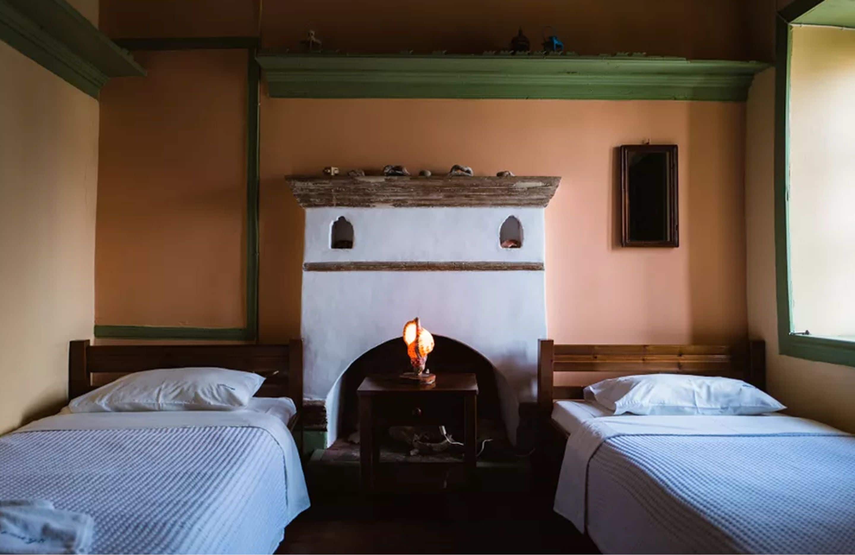 A room with two beds, a fireplace, and a small table with a lamp.