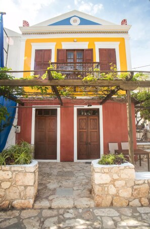 A two-story building with a yellow facade, a balcony with a wooden railing, and a stone entrance. - Karnayo Traditional Houses (Kastellorizo)