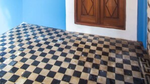 A room with a checkered floor, a wooden door with glass panels, and a ceiling light fixture. - Karnayo Traditional Houses (Kastellorizo)
