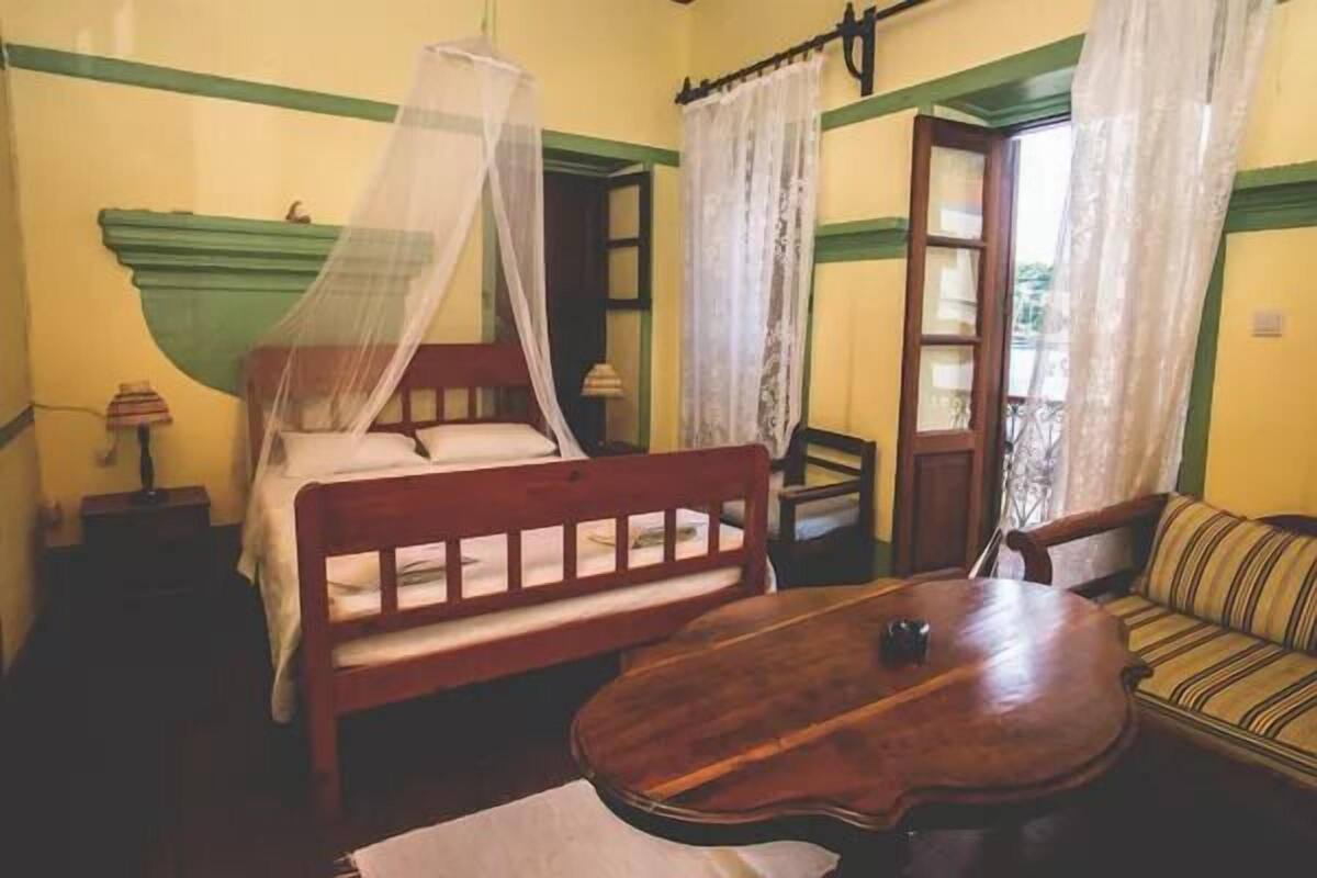 Habitació amb un llit, una taula de fusta, un sofà i una finestra amb cortines.