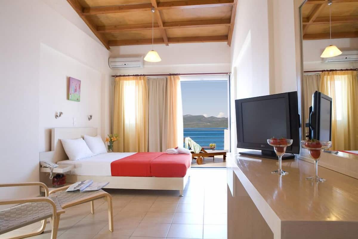 Habitació d'hotel amb un llit, una televisió, una taula petita amb begudes i vista al mar.