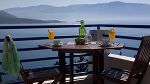 Een balkon met een ontbijttafel, met uitzicht op water en bergen.