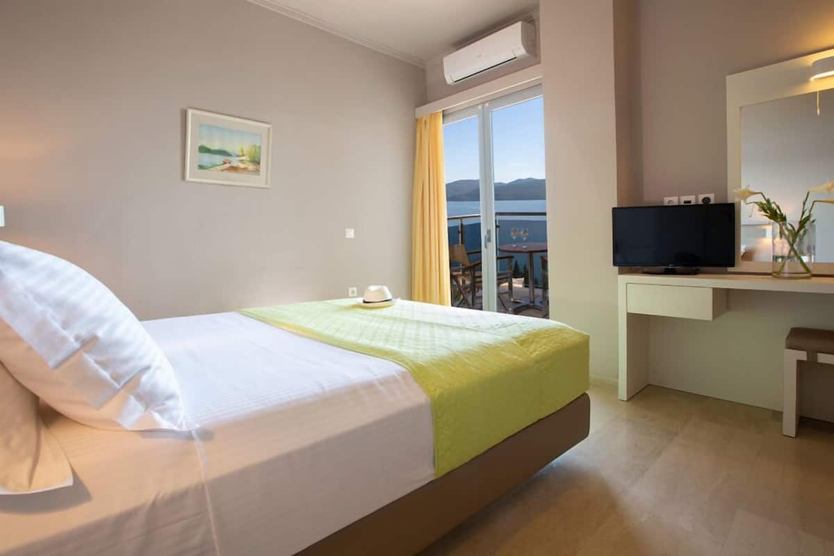 Habitació d'hotel amb un llit, una taula de nit amb televisió, una finestra amb vista al mar i un quadre penjat a la paret.