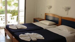 Ein Hotelzimmer mit zwei Betten, einem Holzkopfende, einem Nachttisch und Blick auf Palmen.