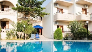 Ein Swimmingpool mit Liegestühlen und Sonnenschirmen, umgeben von mehrstöckigen Gebäuden mit Balkonen und Grünflächen.