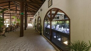 A covered outdoor area with wooden beams, tables, chairs, and a glass display case with items. - Embudu Village (Emboodhoo)