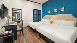 Habitació d'hotel amb dos llits, escriptori, cadira, televisió i una paret blava decorativa.