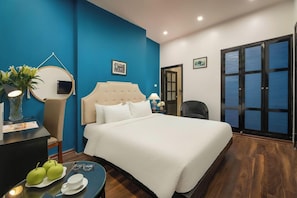 Una camera d'albergo con un letto grande, una scrivania con uno specchio, una sedia e un tavolino con delle mele e una tazza.