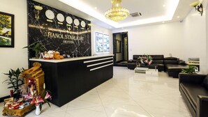 Zona de recepció d'hotel amb un taulell de marbre negre, una làmpada de cristall i sofàs de pell negra.
