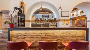 A bar area with a wooden counter, three red chairs, and a variety of bottles and glasses. - Royal Hotel Cortina (Cortina d'Ampezzo)
