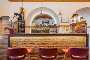 A bar area with a wooden counter, three red chairs, and a variety of bottles and glasses. - Royal Hotel Cortina (Cortina d'Ampezzo)