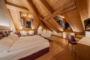A bedroom with a large bed, a desk, and a chair. There is a window with curtains and a view of the outside. - Royal Hotel Cortina (Cortina d'Ampezzo)