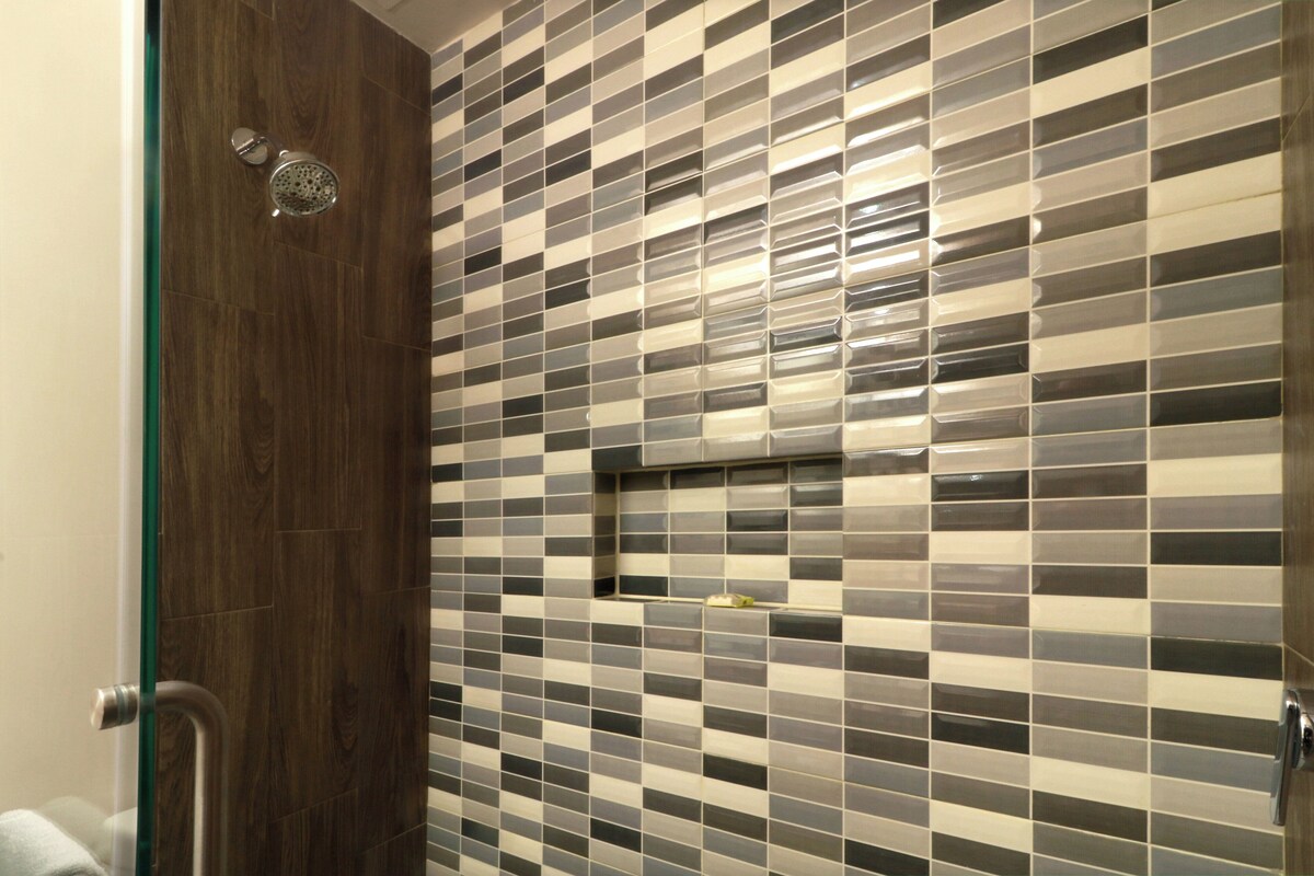 A bathroom with a tiled wall, a wooden door, and a shower.