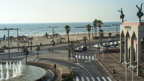 A coastal promenade with a fountain, palm trees, and a beach in the background. - Liber Seashore Suites Aparthotel (Tel Aviv)
