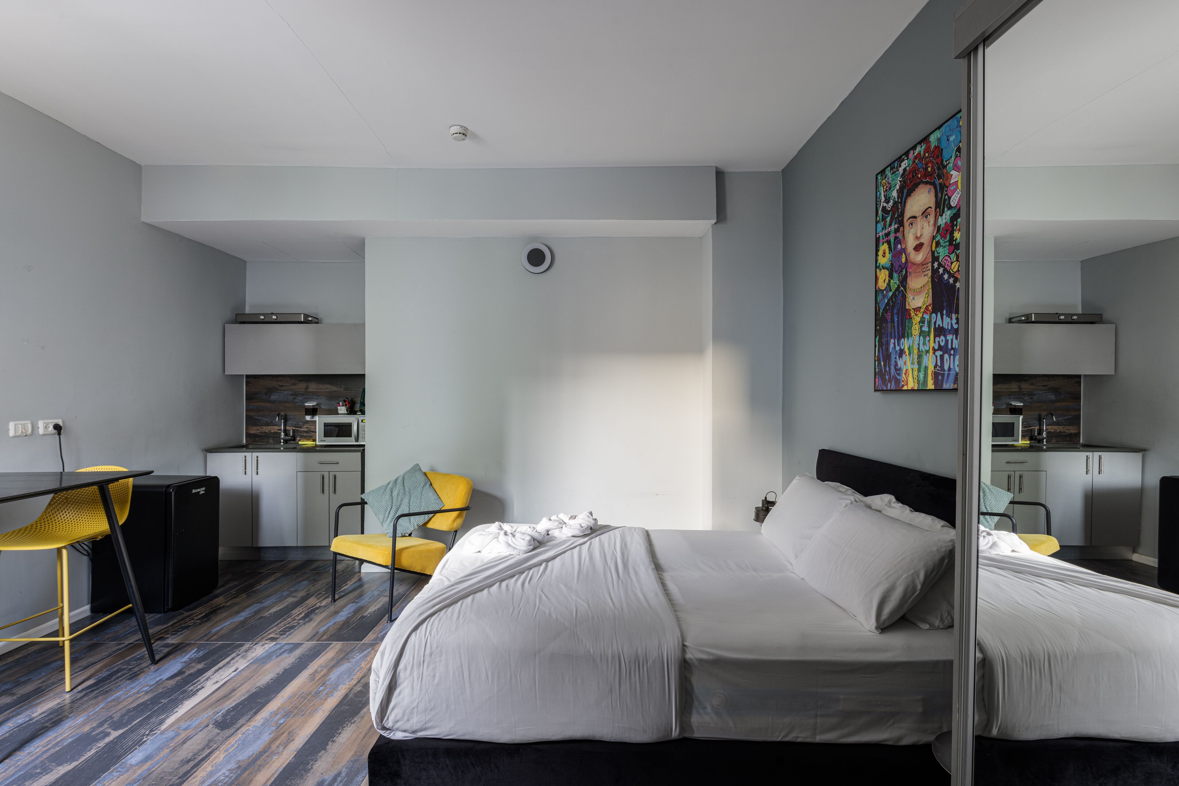A modern hotel room with a large bed, a desk, a chair, and a kitchenette.