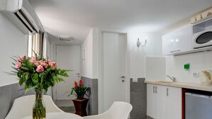 A modern kitchen with white cabinets, a built-in microwave, and a refrigerator. There is a white dining table with chairs, and a vase with flowers on it. - Liber Seashore Suites Aparthotel (Tel Aviv)